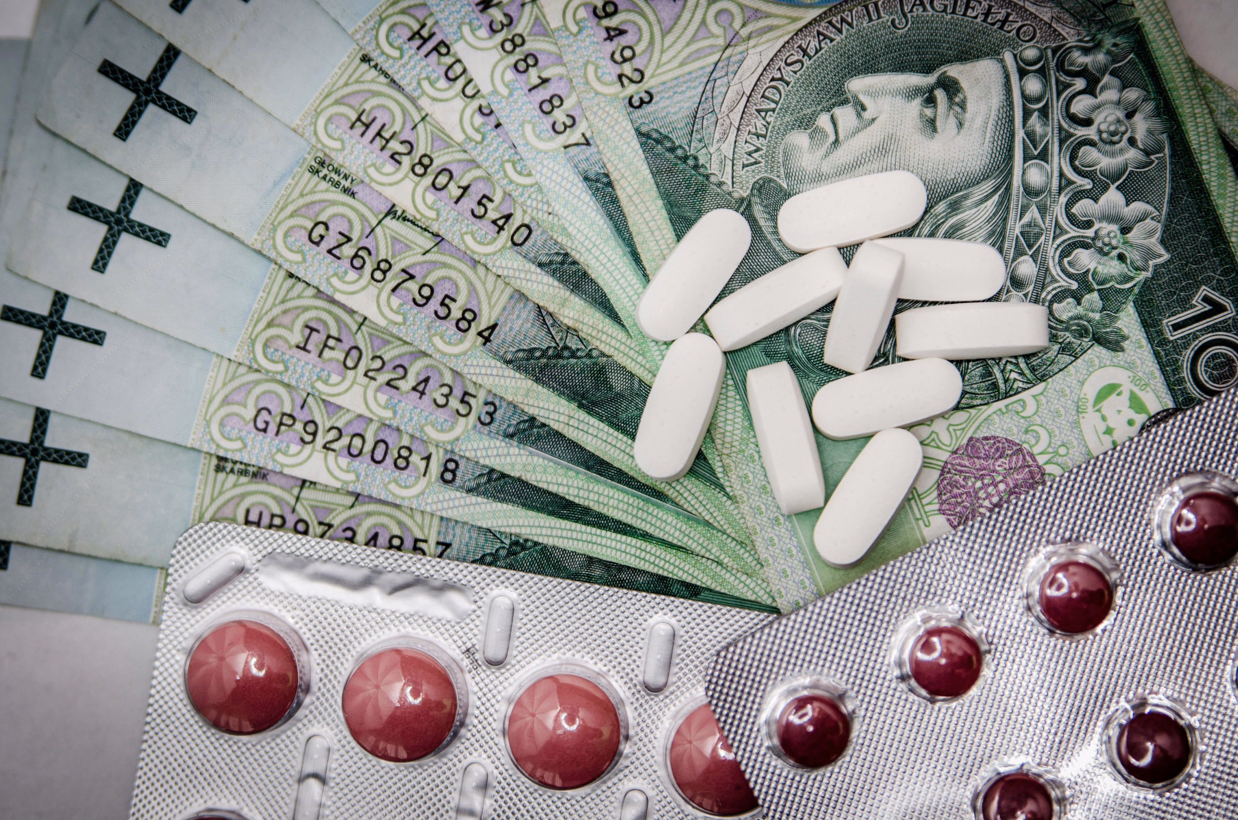 Zdjęcie banknotu stuzłotowego, na nim rozsypane są różne tabletki